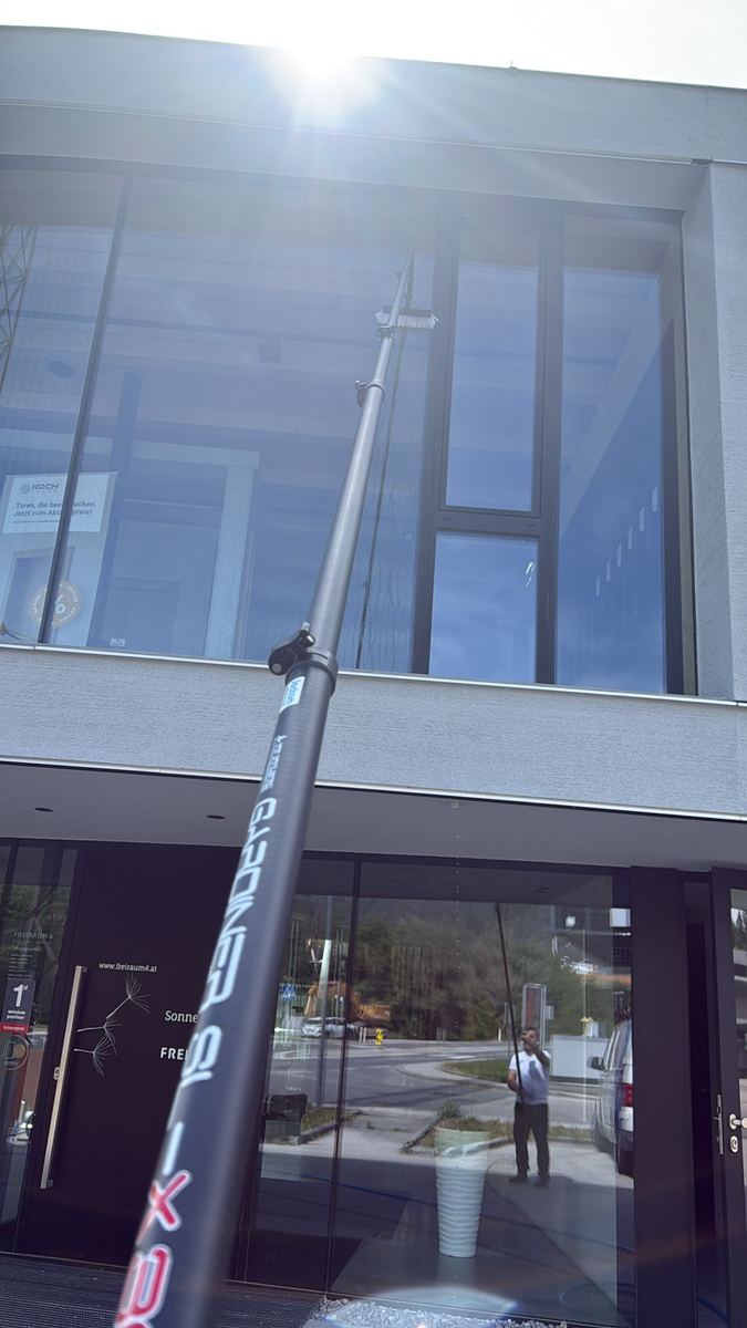 Teleskopstange mit Wasserzuführung reinigt die Glasfassade eines zweigeschossigen Gewerbebaus vom Boden aus